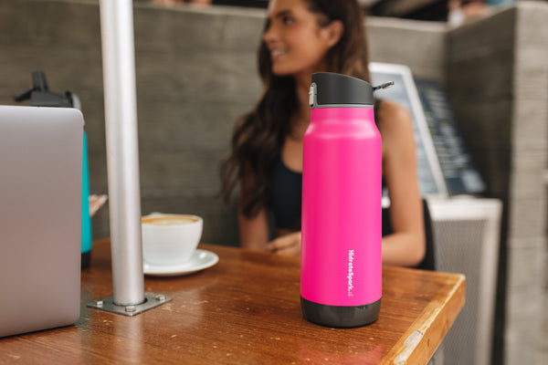 A woman drinking from a pink HidrateSpark bottle.